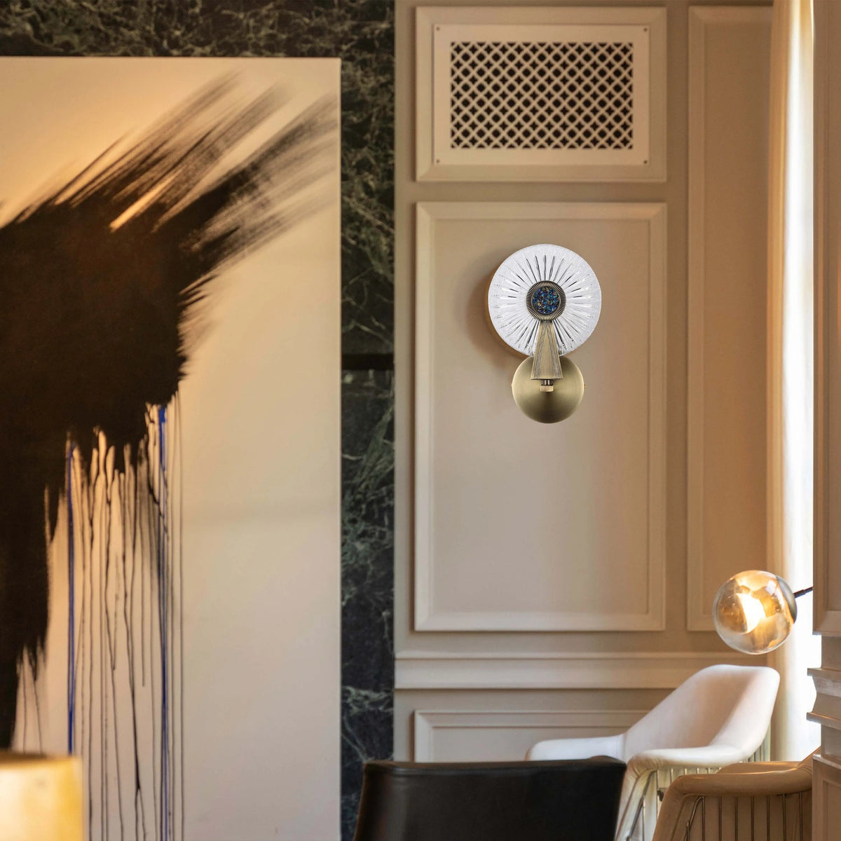An ornate wall light in gold with a decorative glass shade, plus a glowing, suspended spherical light in the background.