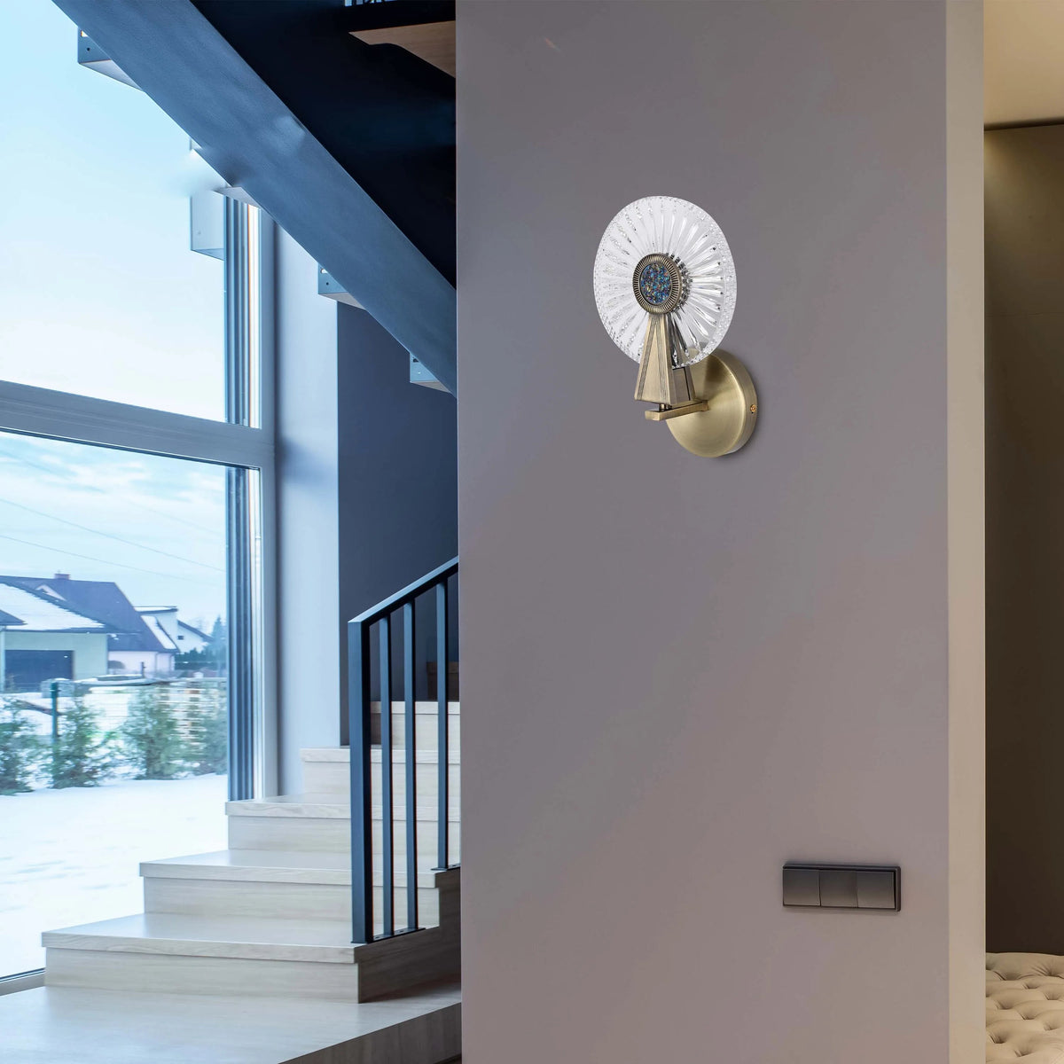 A decorative wall light, featuring a crystal-like design and gold fixture, illuminates a modern hallway with natural light from a window.