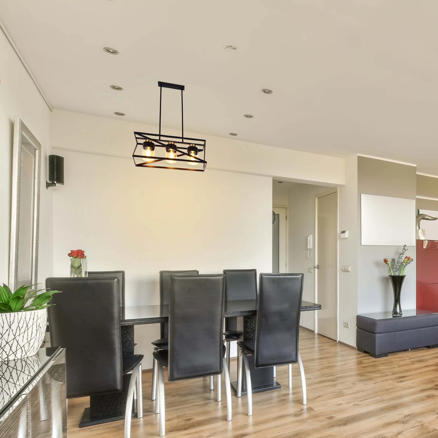A modern chandelier hangs above a dining table, its warm glow contrasting with the sleek, dark chairs and minimalist decor.