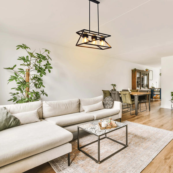 Modern industrial pendant light with three exposed bulbs and a black metal frame, hanging over a living room.