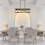 A dining room with modern lighting: a black, linear pendant light hangs above a wooden table, illuminating the space with a warm glow.