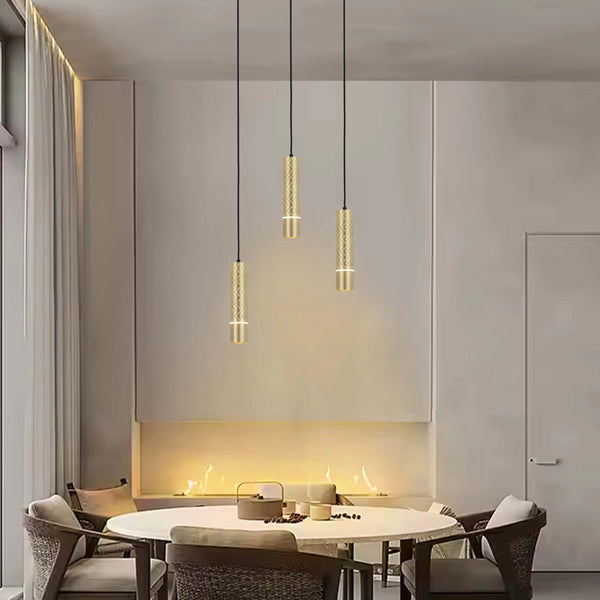 Stylish gold pendant lights hang above a dining table with a lit recessed fireplace behind in a modern dining room.