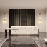 Statement lighting fixtures with gold accents flank a modern reception desk, adding a warm glow to the marble and dark wood backdrop.