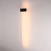 Sleek, modern wall light with a long gold bar and a black rectangular mount, casting a warm glow onto the wall.