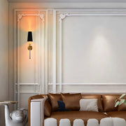 Elegant wall lighting with a black lampshade, gold mount, and clear glass rod emits a warm glow, complementing the classic decor.