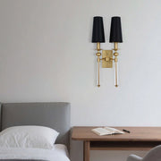 A gold sconce with two black shades, mounted on a light grey wall. Clear glass accents add a touch of elegance to this light fixture.