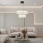A two-tier crystal chandelier illuminates a living space, complemented by recessed ceiling lights and ambient wall lighting.