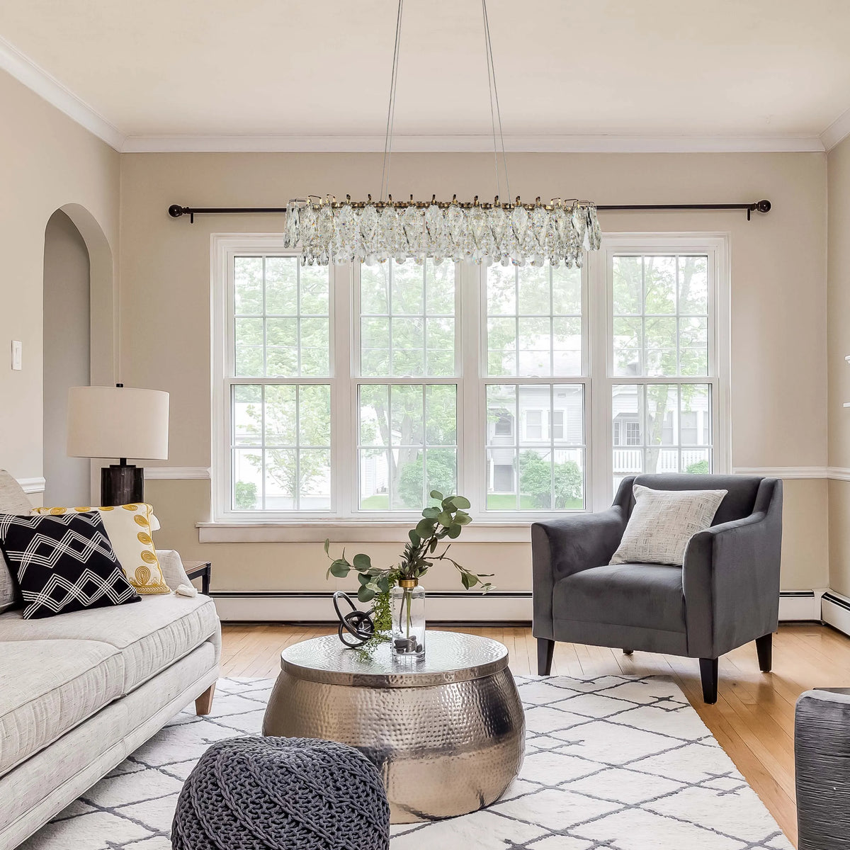 A crystal chandelier hangs in a living room, casting a soft, elegant glow. A table lamp provides additional lighting.