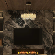 Opulent crystal chandelier hangs above a modern fireplace. Integrated shelf lighting highlights decorative vases.