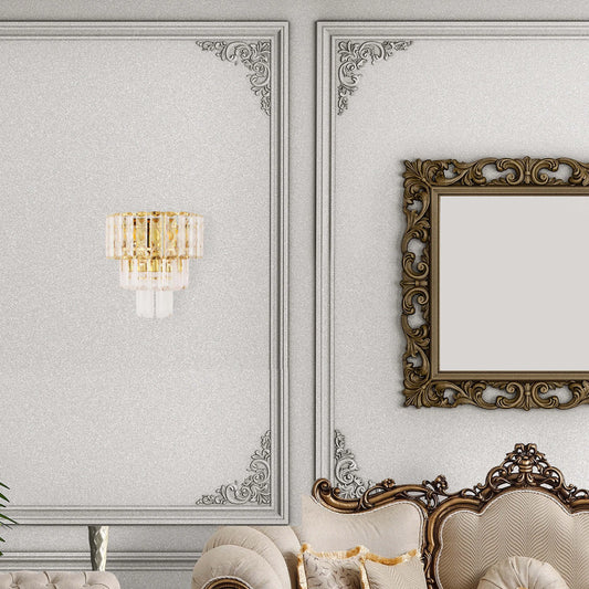 A wall-mounted crystal and gold light fixture exudes luxury, contrasting against the ornate, traditional decor and silver wallpaper.