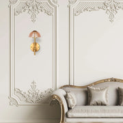 Elegant wall-mounted light fitting with a patterned glass shade and gold-coloured base, illuminating a luxurious interior setting.