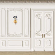A gold and dark grey sconce-style wall light that complements the room's ornate panelling.