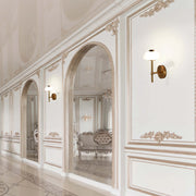 Elegant wall lights illuminate a bright, classic hallway with ornate detailing, arches and a polished floor. Luxury interior design.