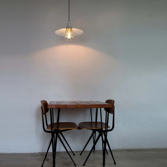 Pendant light shining on a wooden table and chairs. The light creates a warm glow on the wall behind the furniture.