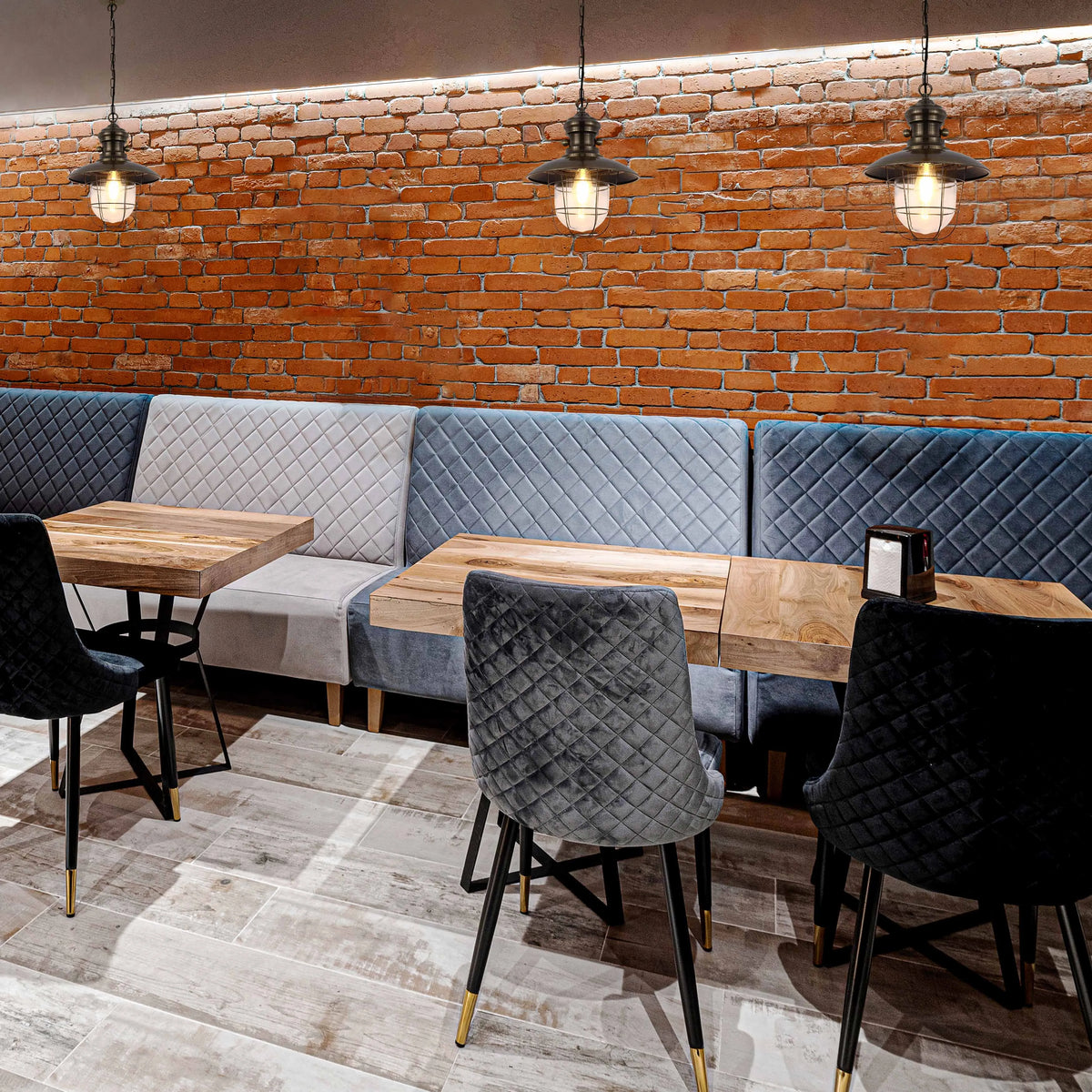 Rustic industrial pendant lights illuminate a cosy restaurant with exposed brick and plush quilted seating.