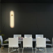 A slim, vertical wall light with a brass centre detail casts a warm glow against the dark wall. Contemporary and stylish lighting.