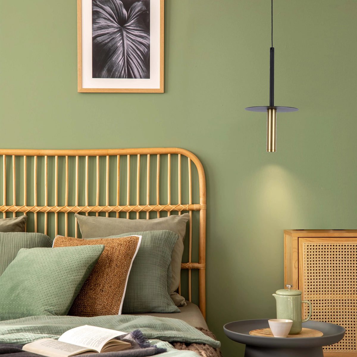 A sleek pendant light fixture with a black and gold finish, casting a warm glow in a stylish bedroom setting.