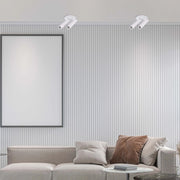 Minimalist white spotlights illuminate a living room with a blank framed poster above a modern sofa and side tables.