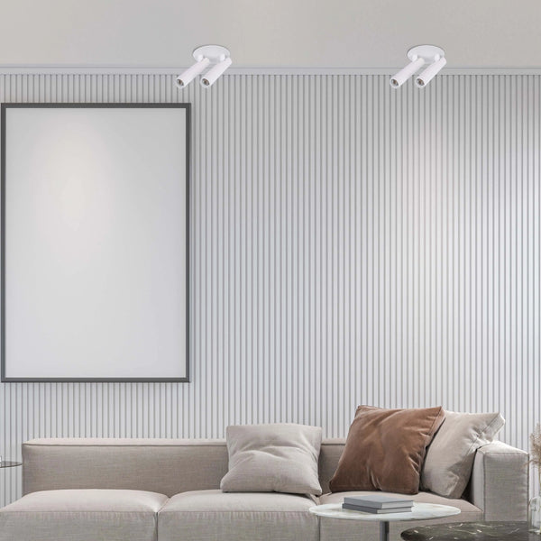 Minimalist white spotlights illuminate a living room with a blank framed poster above a modern sofa and side tables.