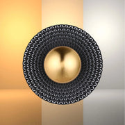 Wall-mounted feature light with black textured surround and a gold, spherical centrepiece. Warm and neutral backdrops.