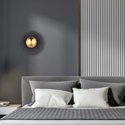 A modern wall light features a central gold sphere surrounded by a geometric, textured disc, adding a touch of contemporary elegance.