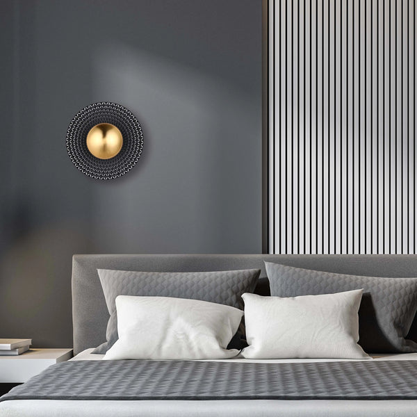 A modern wall light features a central gold sphere surrounded by a geometric, textured disc, adding a touch of contemporary elegance.