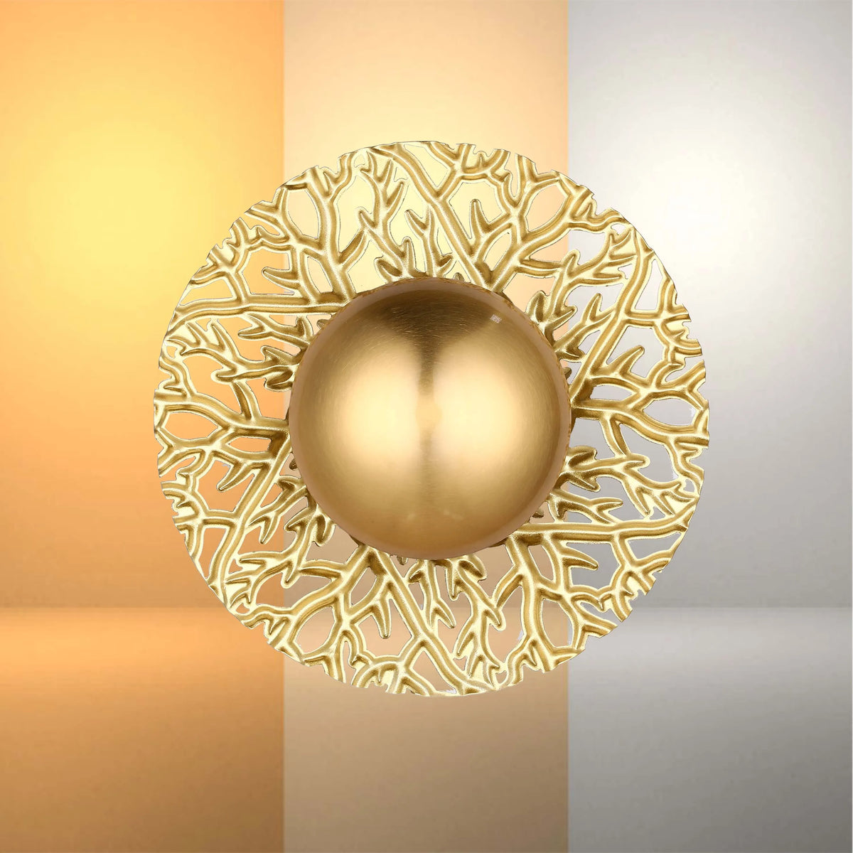 A gold wall light with intricate, organic design and a smooth, spherical centre piece, casting a warm glow on the wall.