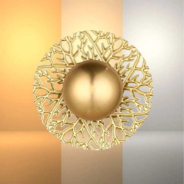 A gold wall light with intricate, organic design and a smooth, spherical centre piece, casting a warm glow on the wall.