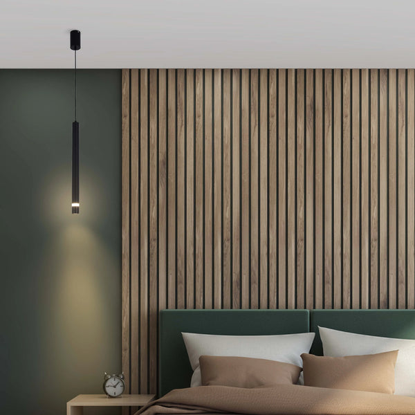 A sleek, black, cylindrical pendant light illuminates the bedside table, casting a warm glow on the green wall and wooden panelling.