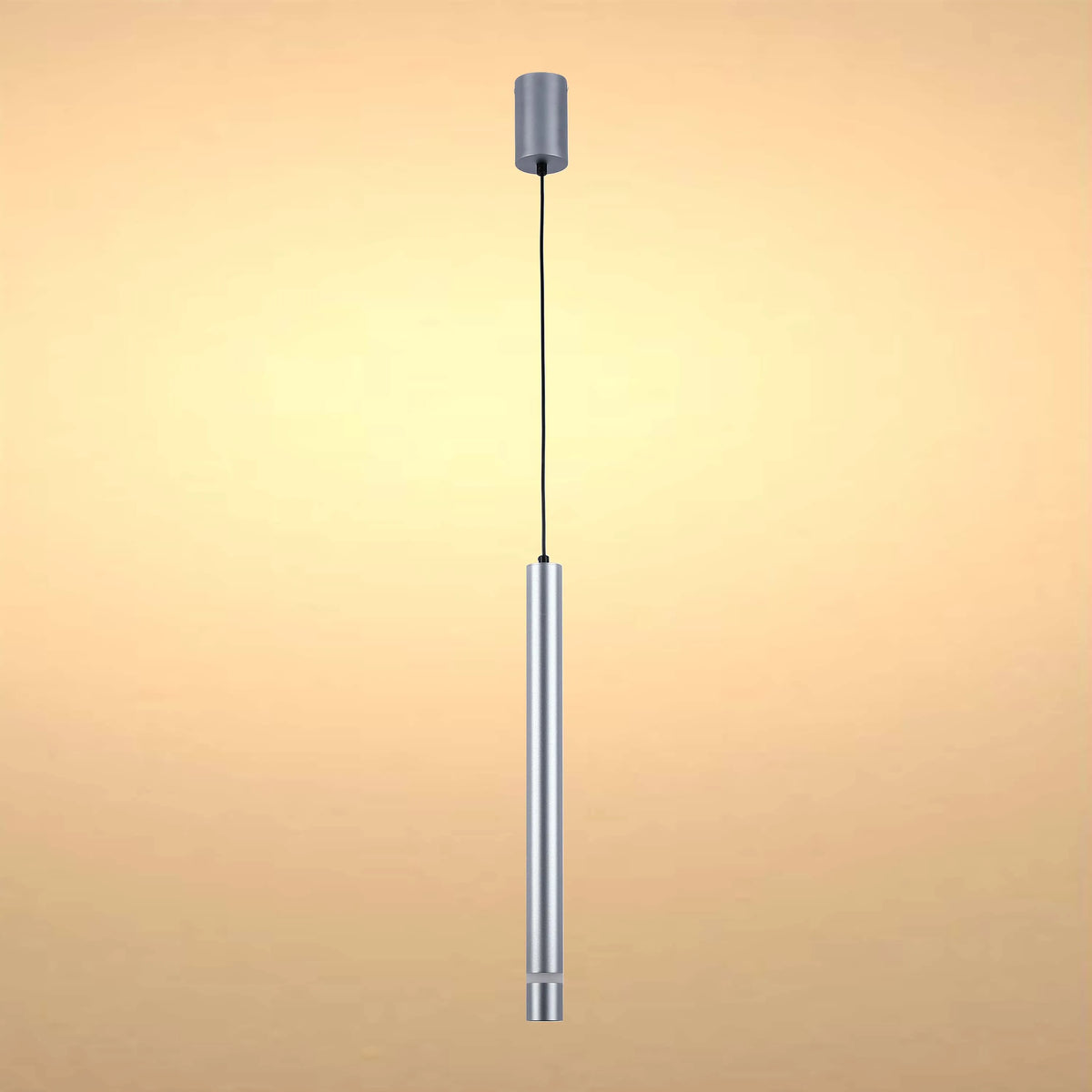 A cylindrical, silver pendant light hangs from a black cable, softly lit against a warm, neutral background.