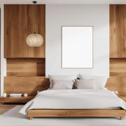 A wicker pendant light hangs above a stylish bedroom, casting a warm glow on the wood and white colour palette.