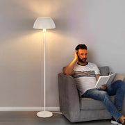 Warm, ambient lighting emanates from a tall floor lamp, creating a cosy reading nook. The lamp has a classic, neutral design.