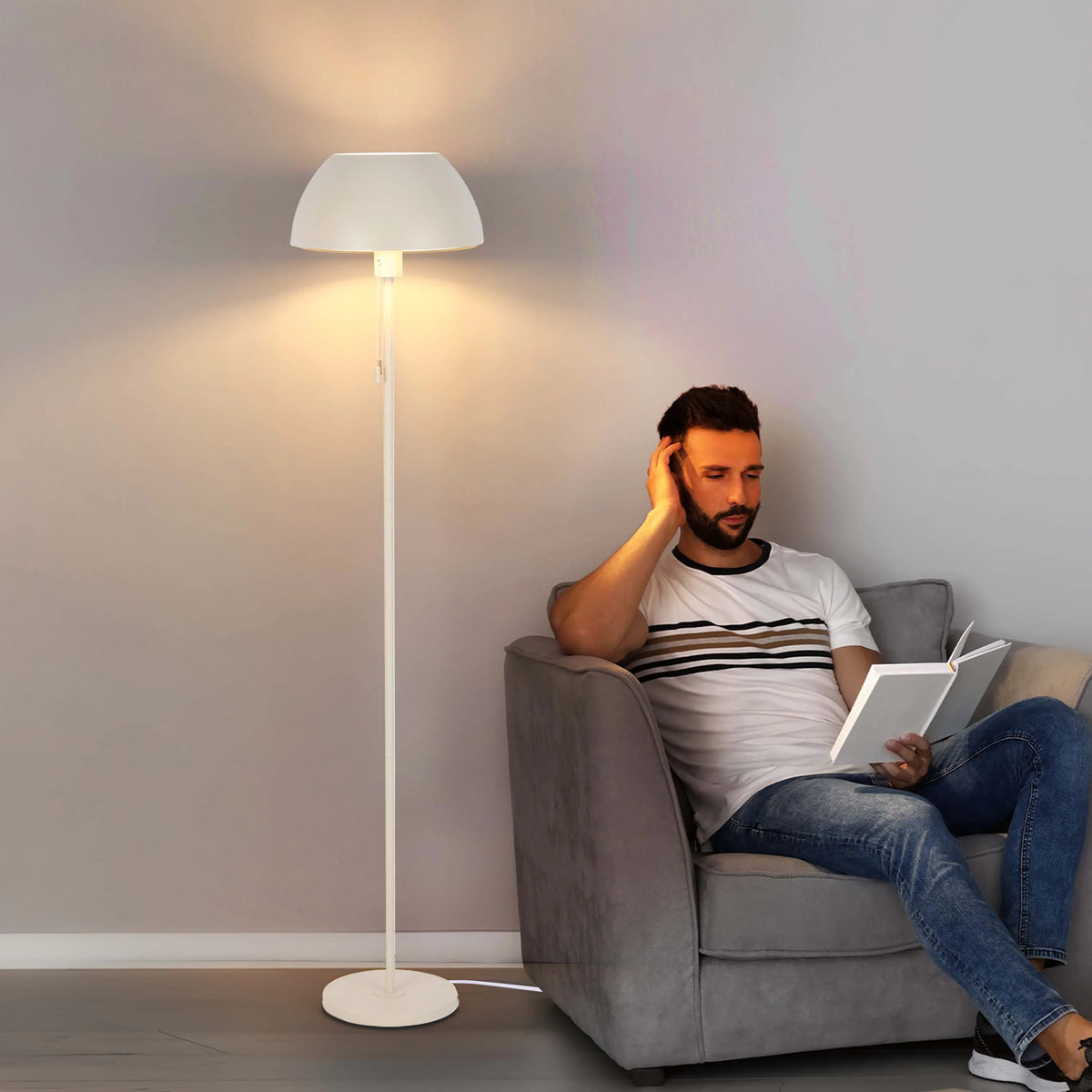 Warm, ambient lighting emanates from a tall floor lamp, creating a cosy reading nook. The lamp has a classic, neutral design.