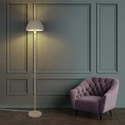 Floor lamp illuminates the room, creating a warm glow against the dark teal walls and highlighting the mauve chair.