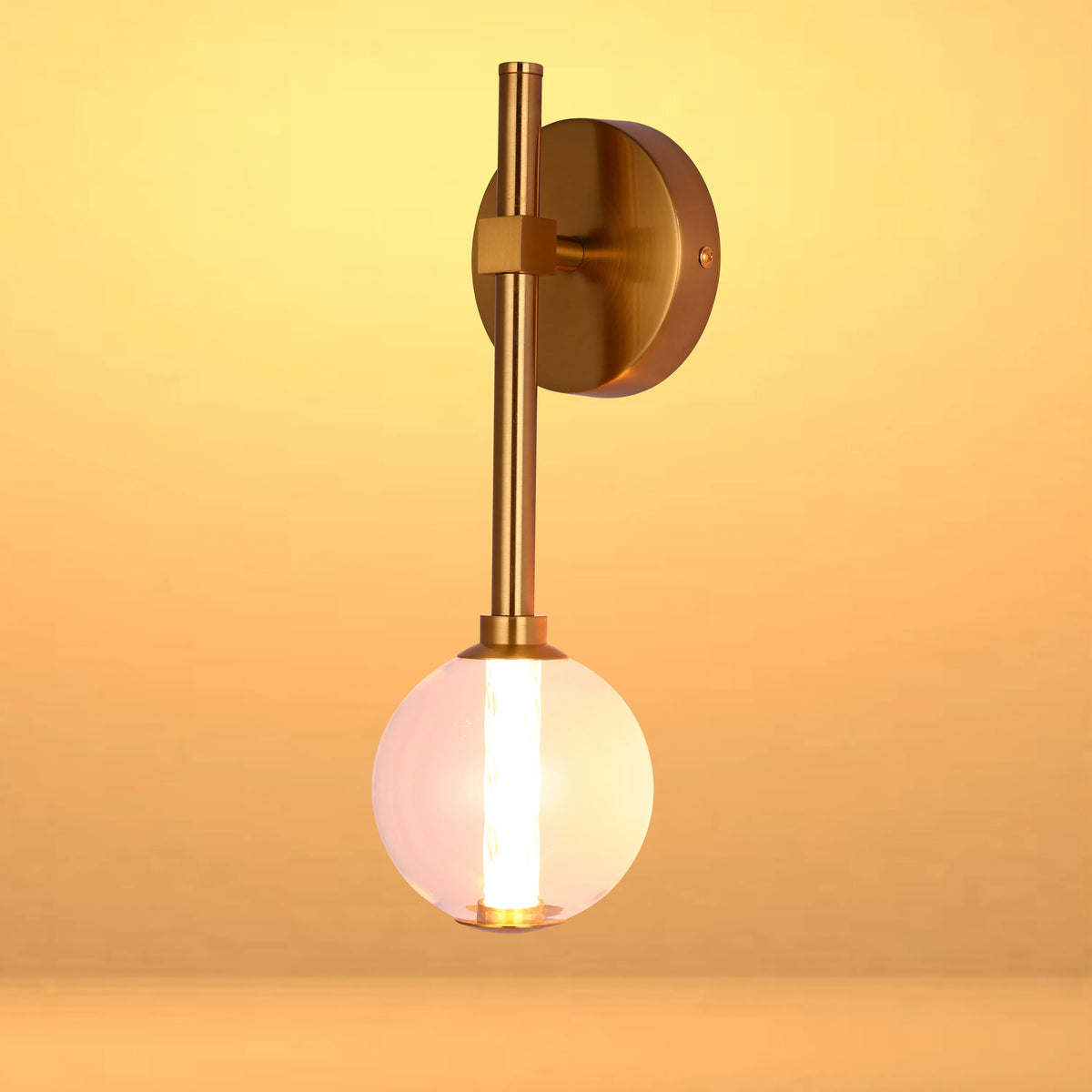 Contemporary wall light with brass fixings and a clear glass globe, illuminating the room with a warm glow.