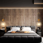 Bedroom with ambient lighting. Wall-mounted sconces flank a large, upholstered bed against a wood panelled wall.