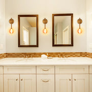A bathroom with two brown-framed mirrors and three globe-shaped vanity lights.