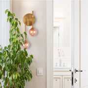 A stylish wall light with a brass finish and two pink glass globes, creating a warm and inviting atmosphere.
