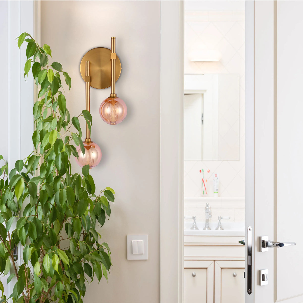 A stylish wall light with a brass finish and two pink glass globes, creating a warm and inviting atmosphere.