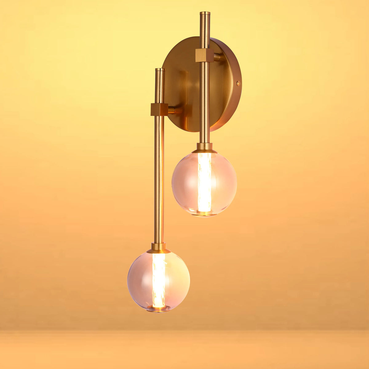 Contemporary brass wall light with two illuminated glass globe shades, casting a warm glow.