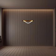 Modern, curved wall light with a brass fixture emitting a warm, ambient glow. Stylish interior lighting.