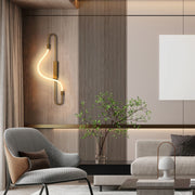 A statement wall light with a curved design casts a warm glow in this modern interior, complemented by hidden ambient lighting.