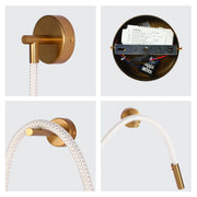 A gold, modern wall sconce with a white, braided cord. The lighting features a sleek and minimalist design.