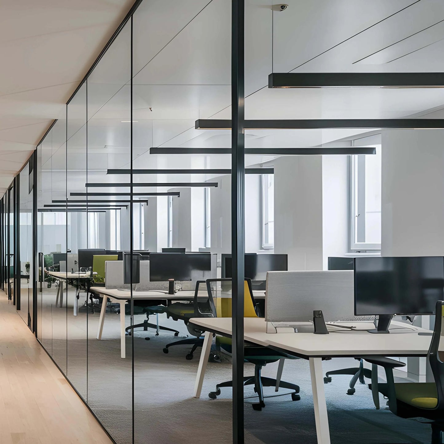 Contemporary office lighting: sleek, linear fixtures suspended above modern workstations in a glass-walled office space.