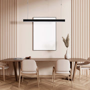A sleek, modern black pendant light hangs above a wooden dining table with neutral chairs, adding a touch of sophistication to the room.