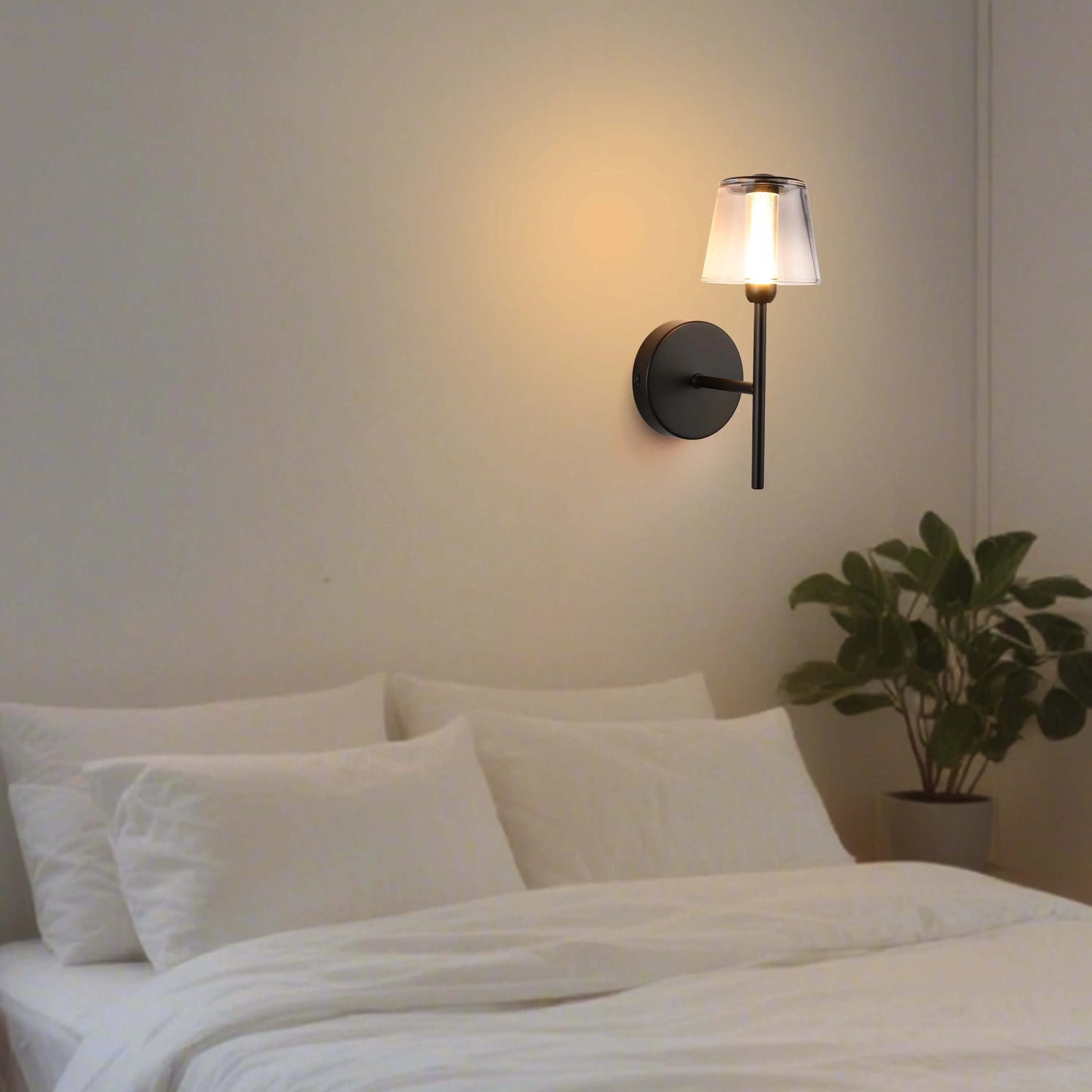 Wall mounted light with a clear glass shade, emitting a warm glow in a bedroom setting.