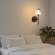 Wall mounted light with a clear glass shade, emitting a warm glow in a bedroom setting.