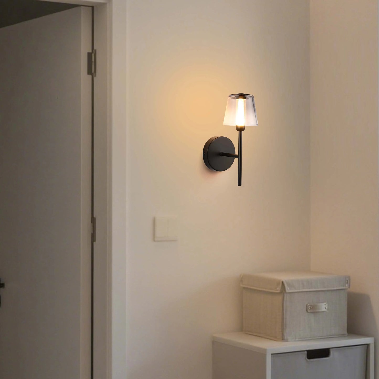 Illuminated wall sconce with a sleek, modern design. It emits a warm, inviting glow against a neutral wall.