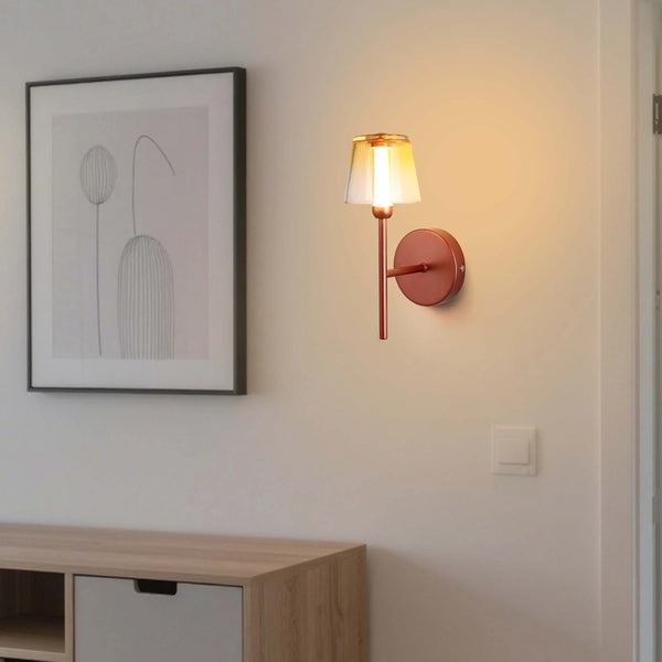 Modern wall light with a clear glass shade and a warm, inviting glow, mounted on a neutral wall, creating a cosy ambiance.