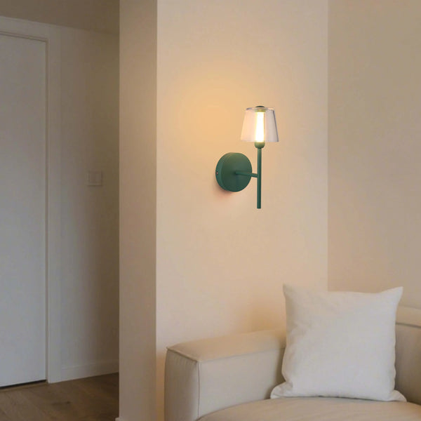 A stylish green wall light with a clear shade emits a warm, inviting glow, adding a touch of modern elegance to any interior.